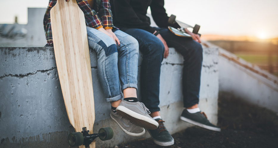 Picture of teens sitting on a wall with a skateboard